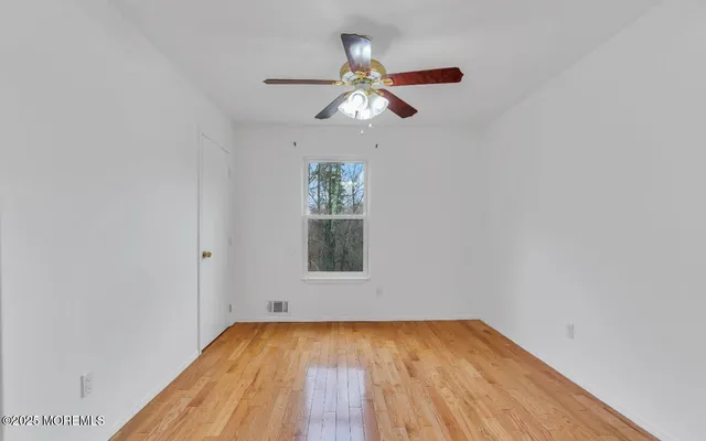 an empty room with wooden floor chandelier fan and windows