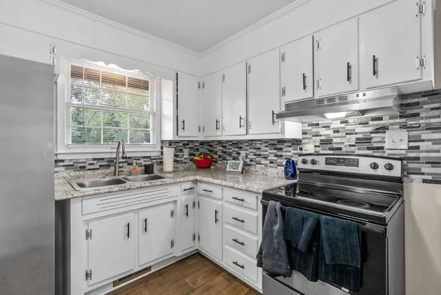a kitchen with white cabinets appliances a sink and a window