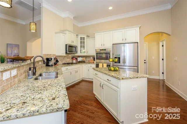 a kitchen with stainless steel appliances granite countertop a stove top oven a refrigerator a sink and dishwasher with wooden floor