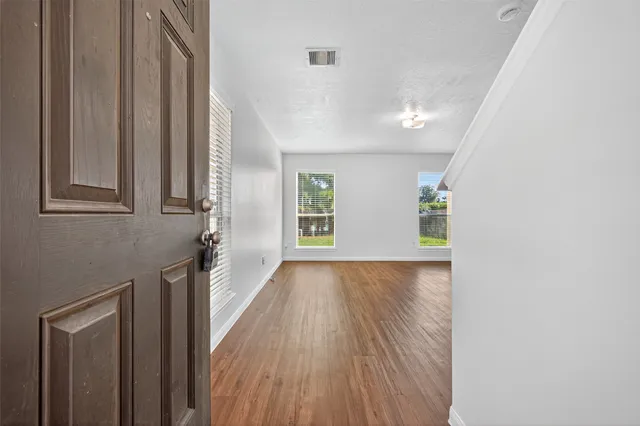 a view of an empty room with wooden floor and a window