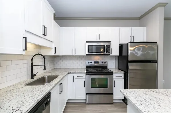 a kitchen with granite countertop a sink stainless steel appliances and white cabinets