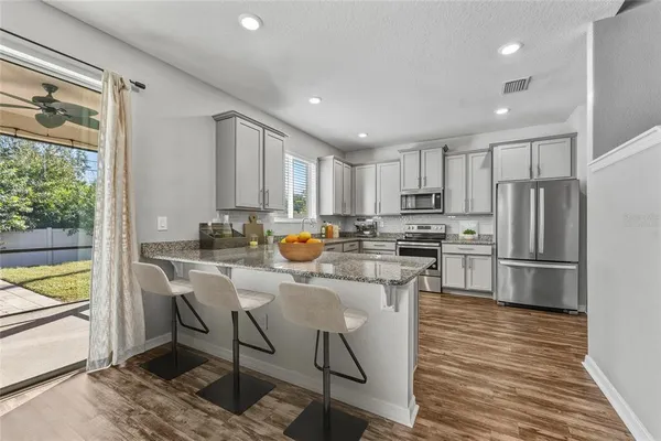 a kitchen with stainless steel appliances granite countertop a refrigerator a stove a sink a island and chairs with wooden floor