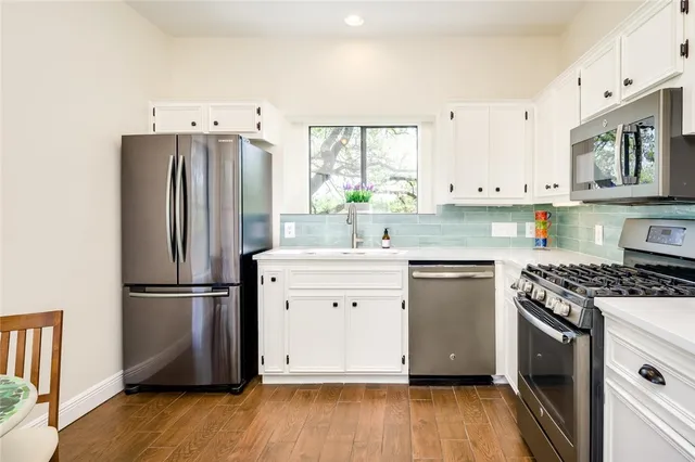 a kitchen with white cabinets stainless steel appliances and wooden floor