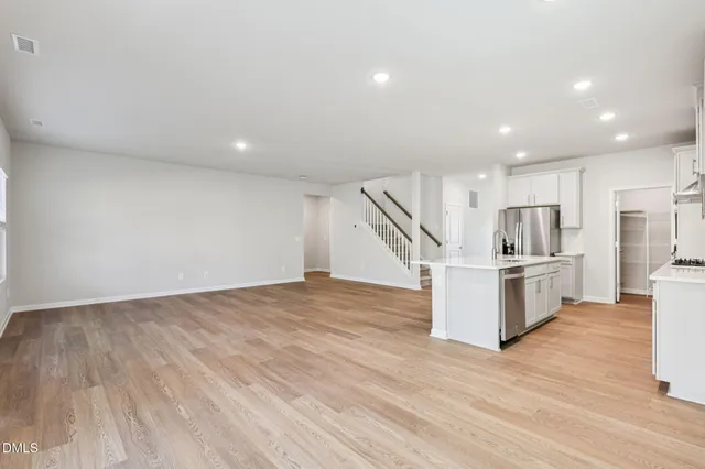 a view of an empty room with wooden floor and kitchen