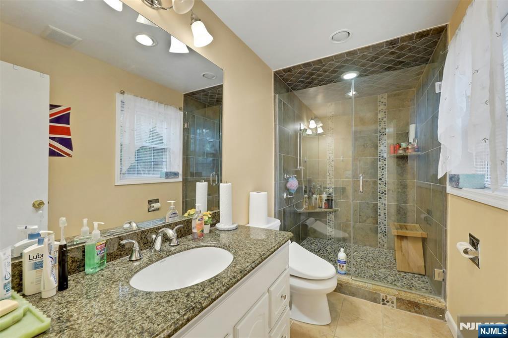 1093 Sheridan Street New Milford, NJ 07646 - Photo 22 of 45 a bathroom with a granite countertop sink toilet a mirror a vanity and shower