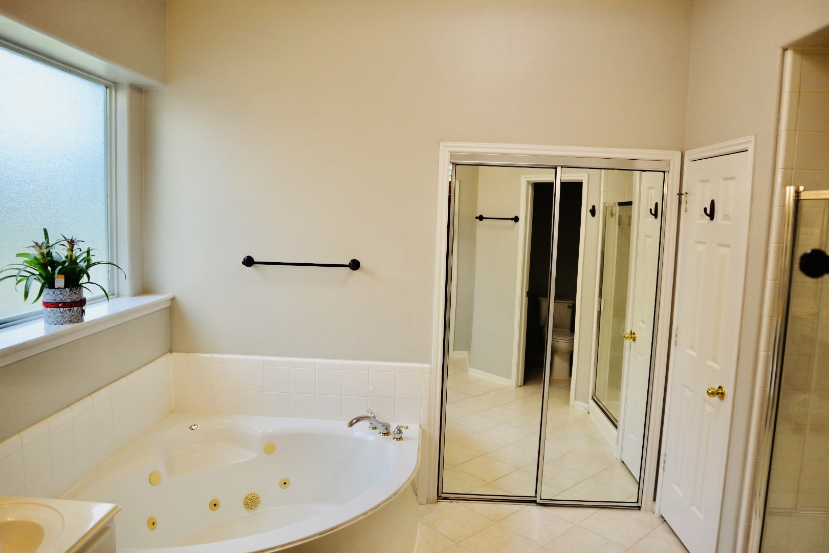 19114 Emory Trail Spring, TX 77388 - Photo 17 of 32 Spacious bathroom with a large corner jacuzzi tub, mirrored closet doors, and a separate shower. Natural light streams in through a frosted window, enhancing the neutral decor.