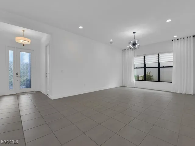 an empty room with chandelier fan and windows