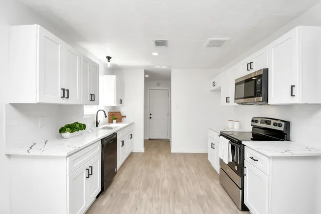 a kitchen with stainless steel appliances a white stove top oven a sink a refrigerator white cabinets and wooden floor