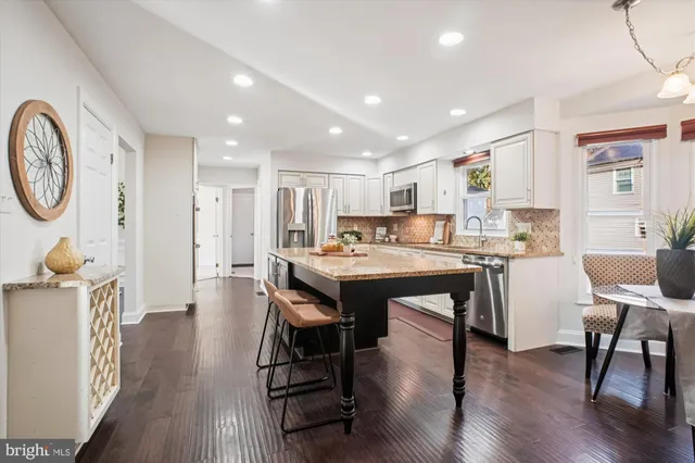 a kitchen with stainless steel appliances granite countertop wooden cabinets a sink a stove a refrigerator and island with wooden floor