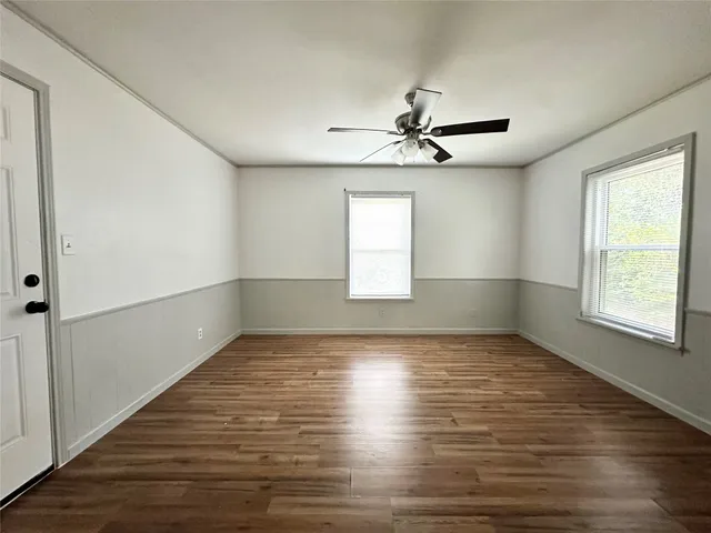 an empty room with wooden floor chandelier fan and windows