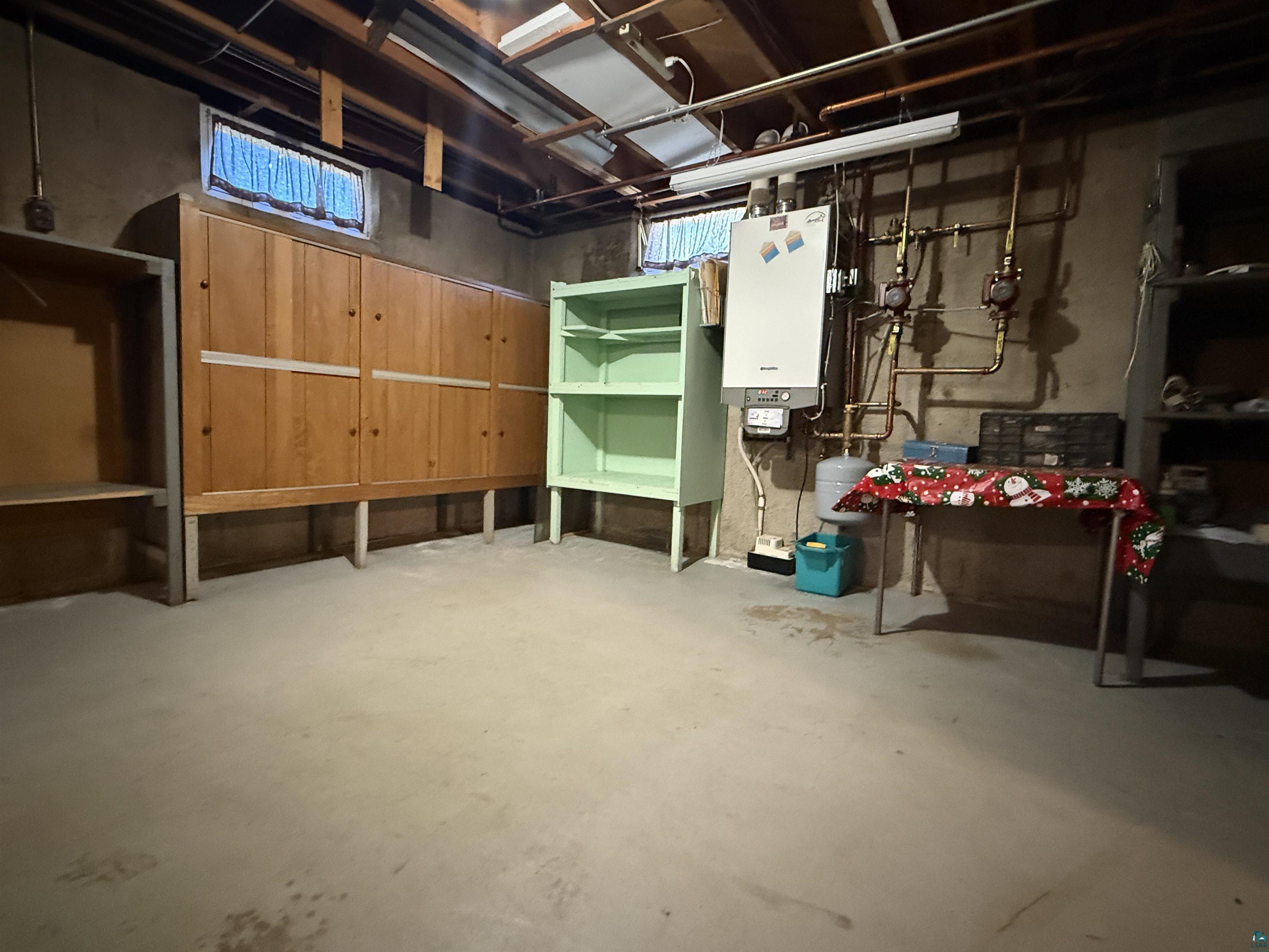 607 3rd Street Northeast Chisholm, MN 55719 - Photo 26 of 32 Basement utility space featuring a concrete floor, exposed ceiling joists, a compact water heater, and a small window