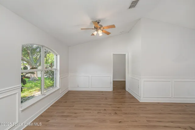 an empty room with wooden floor fan and windows