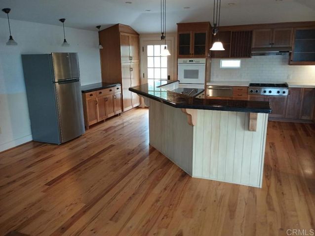 a kitchen with stainless steel appliances granite countertop a refrigerator a sink dishwasher a stove and a wooden floors