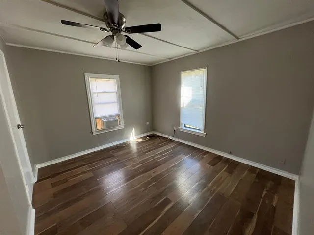 an empty room with wooden floor chandelier fan and windows