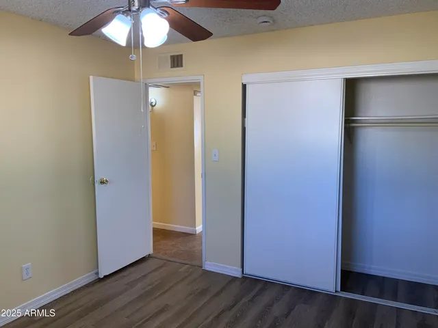 a view of an empty room with wooden floor and a ceiling fan