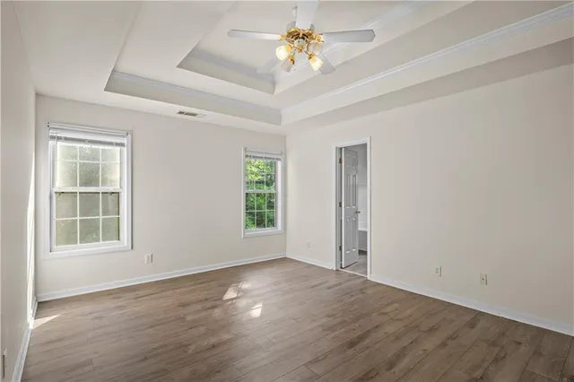 an empty room with wooden floor chandelier fan and windows
