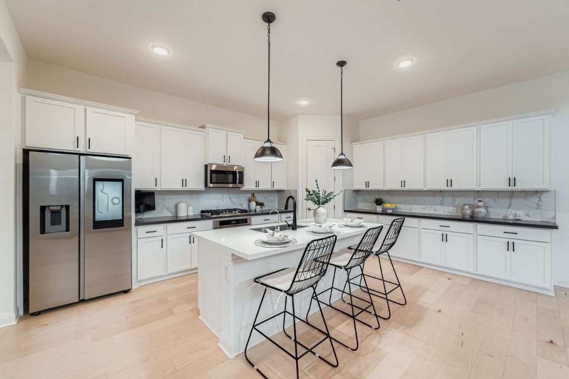 2928 Birdcall Path Leander, TX 78641 - Photo 12 of 36 a kitchen with stainless steel appliances kitchen island a table chairs sink and cabinets