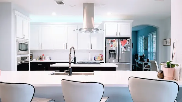 a living room with stainless steel appliances furniture a chandelier and a kitchen view
