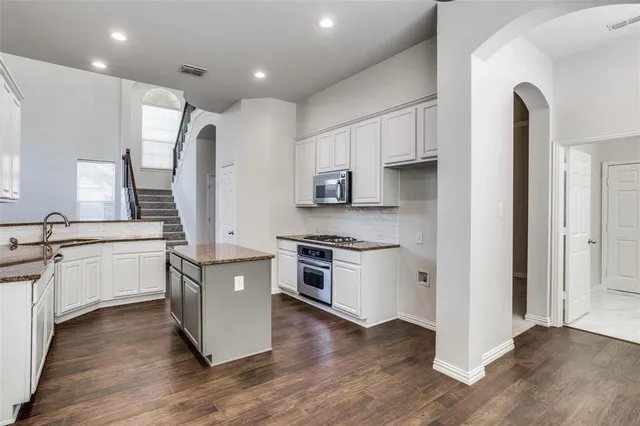 a kitchen with stainless steel appliances granite countertop a refrigerator a sink dishwasher a stove and white cabinets with wooden floor