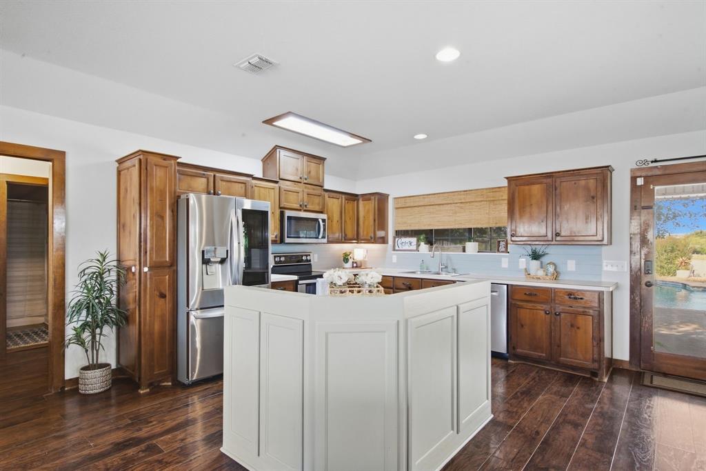 950 Johnson Bend Road Weatherford, TX 76088 - Photo 16 of 40 Kitchen featuring wood-finish flooring, white paneled island, wood cabinetry, stainless steel appliances, and a light blue subway tile backsplash