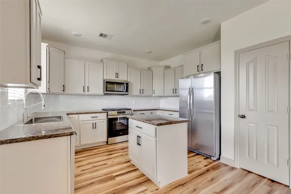 a kitchen with stainless steel appliances granite countertop a refrigerator a stove top oven a sink and dishwasher with wooden floor
