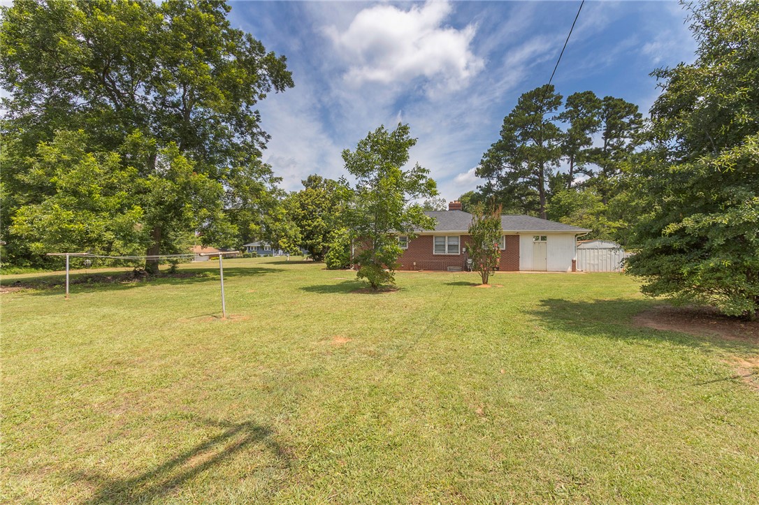 1218 Bolt Drive Anderson, SC 29621 - Photo 41 of 46 A deep grassy yard stretches behind the brick-clad residence, enveloped by mature trees under an azure sky.