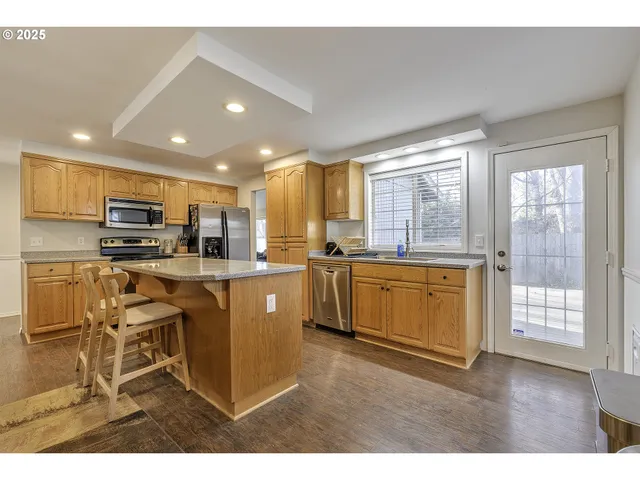 a kitchen with stainless steel appliances kitchen island granite countertop a stove a sink a refrigerator white cabinets and a dining table with wooden floor