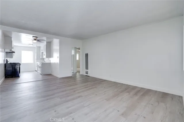 a view of empty room with wooden floor and kitchen view