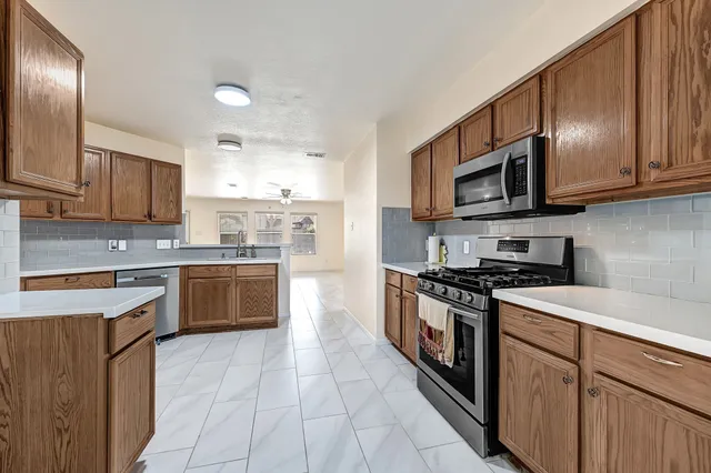 a kitchen with stainless steel appliances granite countertop a stove top oven a sink dishwasher and a refrigerator with wooden cabinets