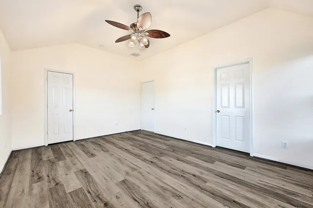 an empty room with wooden floor fan and windows