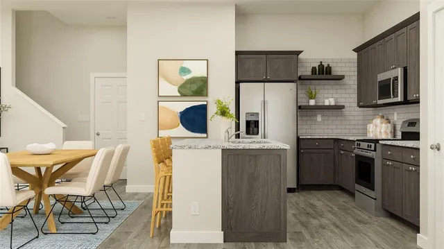 a kitchen with stainless steel appliances granite countertop a stove top oven a sink a refrigerator a dining table and chairs with wooden floor