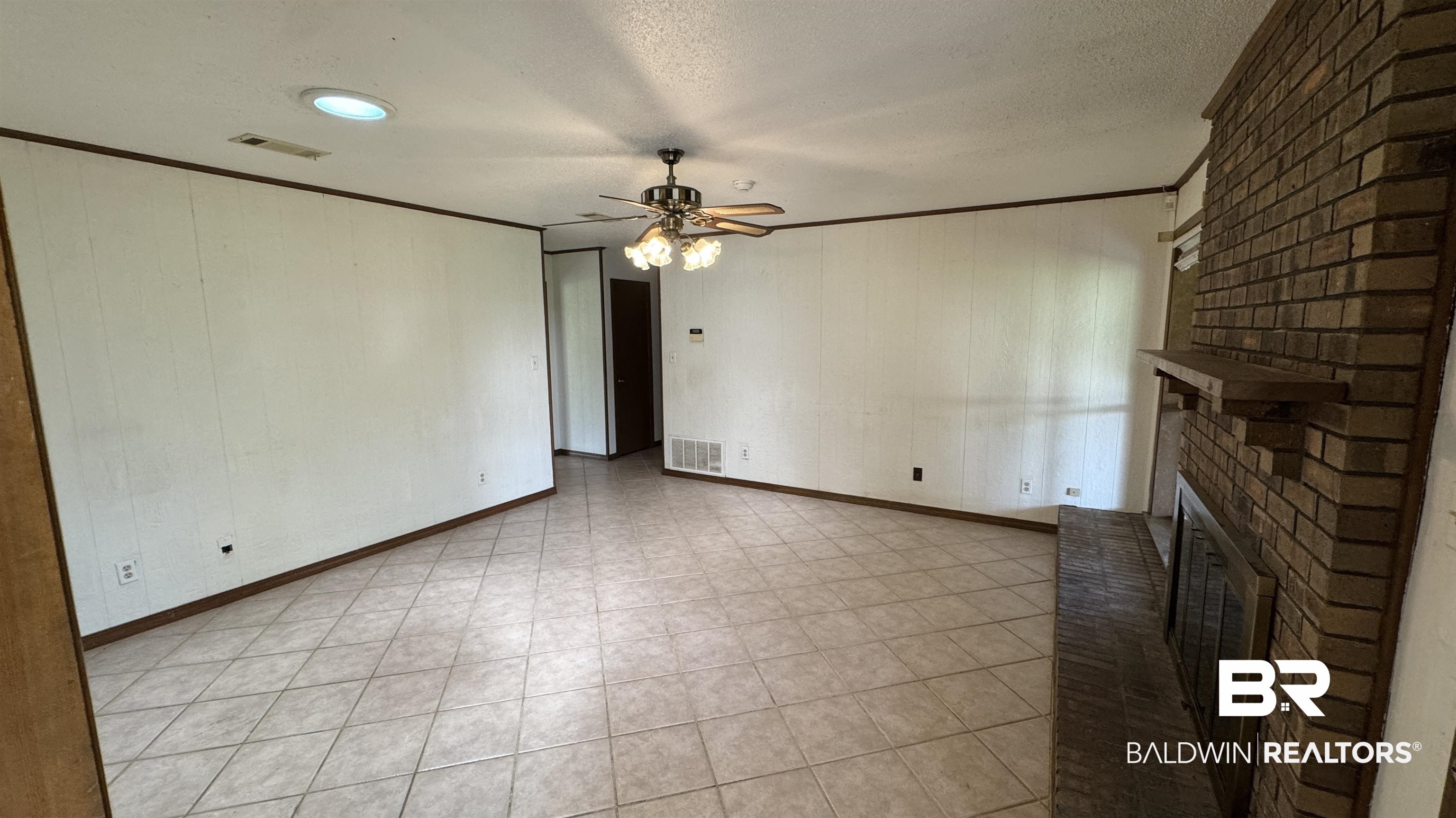 33370 Highway 98 Lillian, AL 36549 - Photo 26 of 58 Spacious living area featuring neutral tile flooring, a prominent brick fireplace with hearth, and a ceiling fan with integrated lighting