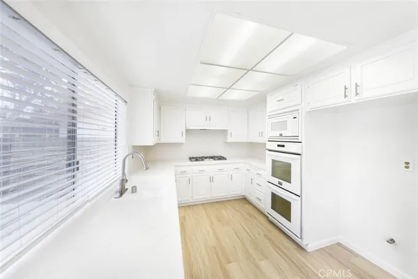 a large white kitchen with kitchen island a large window a sink and cabinets