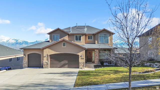 Traditional-style house with stucco siding, a front yard, concrete driveway, a mountain view, and an attached garage