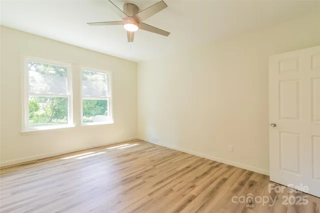 an empty room with wooden floor fan and windows