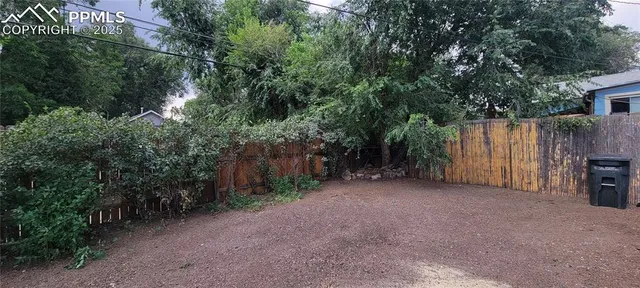a view of a backyard with large trees and wooden fence