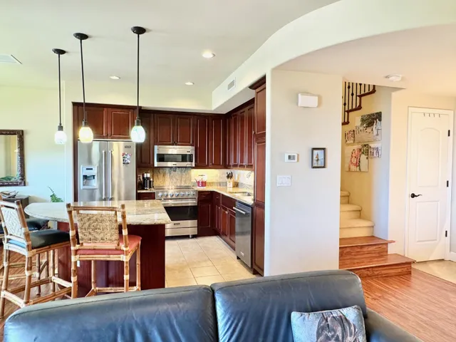 a kitchen with stainless steel appliances granite countertop a refrigerator a sink dishwasher a stove and a dining table with wooden floor