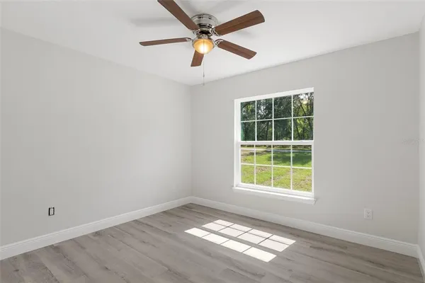 an empty room with wooden floor ceiling fan and windows