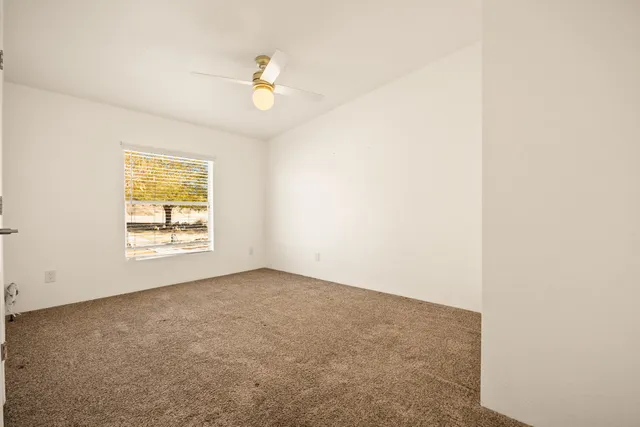 an empty room with a ceiling fan and carpet