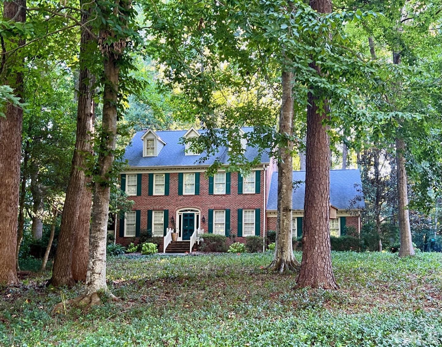 a view of a brick house with a yard and large trees