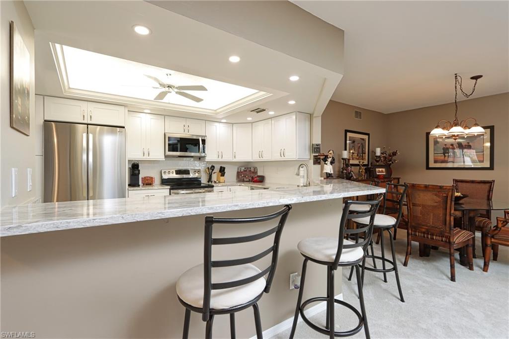 661 Windsurf Lane, Unit A103 Naples, FL 34108 - Photo 6 of 18 a kitchen with stainless steel appliances granite countertop a stove a sink a refrigerator with a dining table and chairs