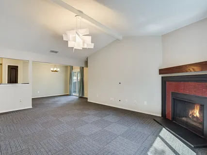 a view of an empty room with kitchen and fireplace