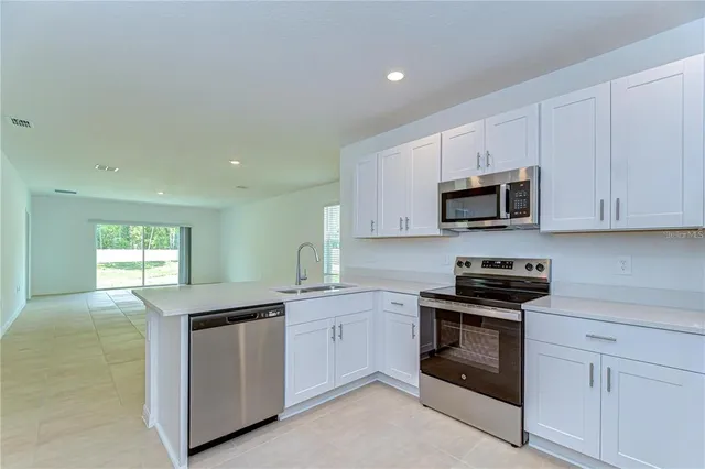 a kitchen with stainless steel appliances granite countertop white cabinets a sink a stove a window and white