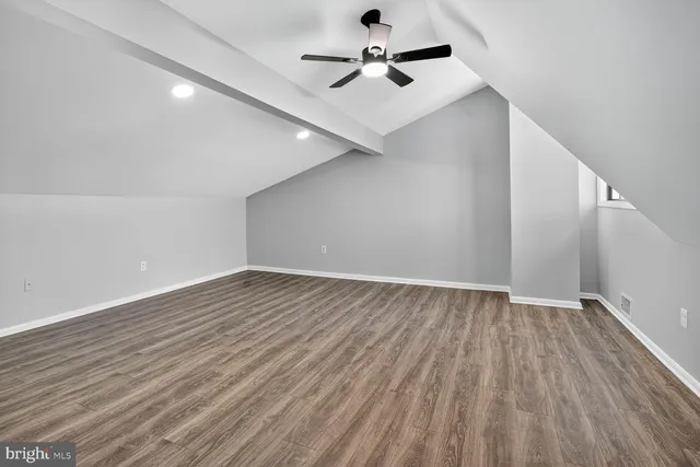 a view of an empty room with wooden floor and a ceiling fan