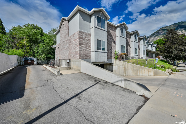 677 300 North, Unit 7 Provo, UT 84606 - Photo 1 of 16 Multi-level building exterior featuring stone-look and stucco siding, multiple windows, and a paved driveway leading to a lower-level entrance