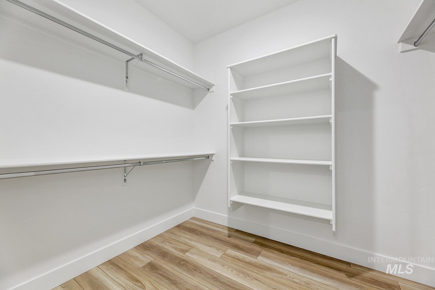 4548 West Wapoot Street Meridian, ID 83646 - Photo 16 of 17 Walk-in closet featuring white walls, wood-finish flooring, two levels of shelving with hanging rods, and an additional built-in shelving unit