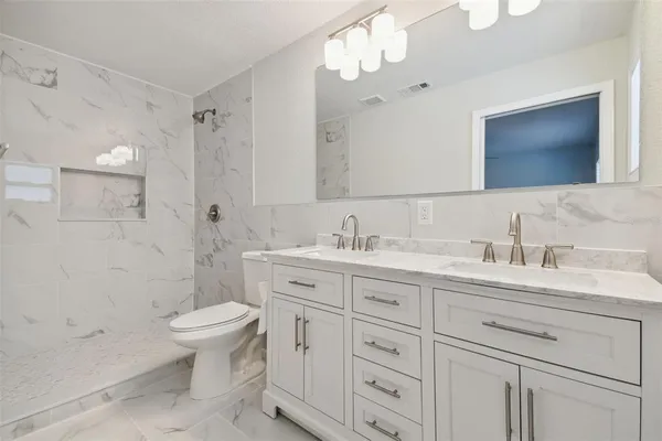 a bathroom with double vanity sink a toilet a mirror and shower