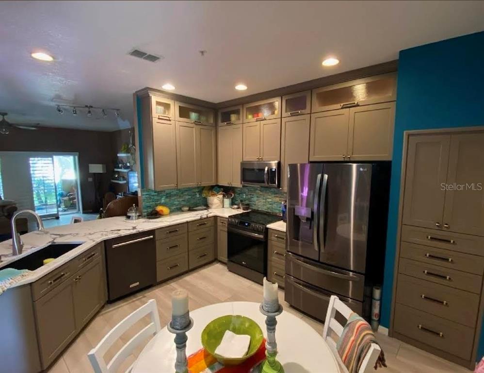 11229 Kapok Grand Circle Madeira Beach, FL 33708 - Photo 4 of 23 a open kitchen with stainless steel appliances granite countertop a refrigerator a sink a stove and chairs with wooden floor