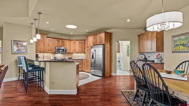 a kitchen with stainless steel appliances kitchen island granite countertop a refrigerator a stove a sink a dining table and chairs with wooden floor