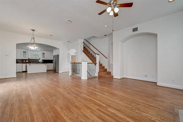 a view of an empty room with wooden floor a ceiling fan and kitchen space
